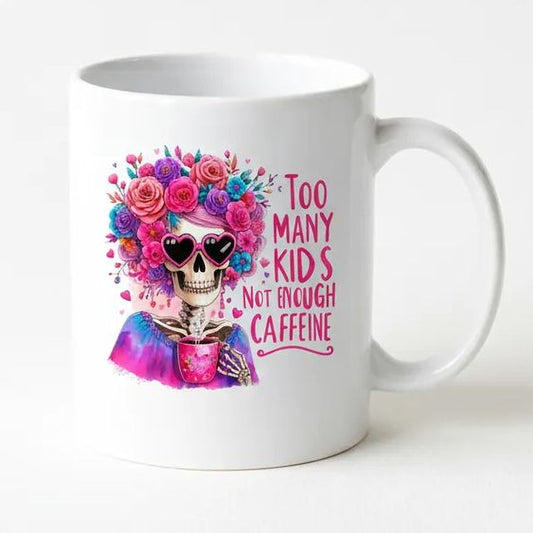 A white ceramic mug with a colorful illustration of a skeleton wearing sunglasses and a flower crown, along with the text "Too many kids not enough caffeine".