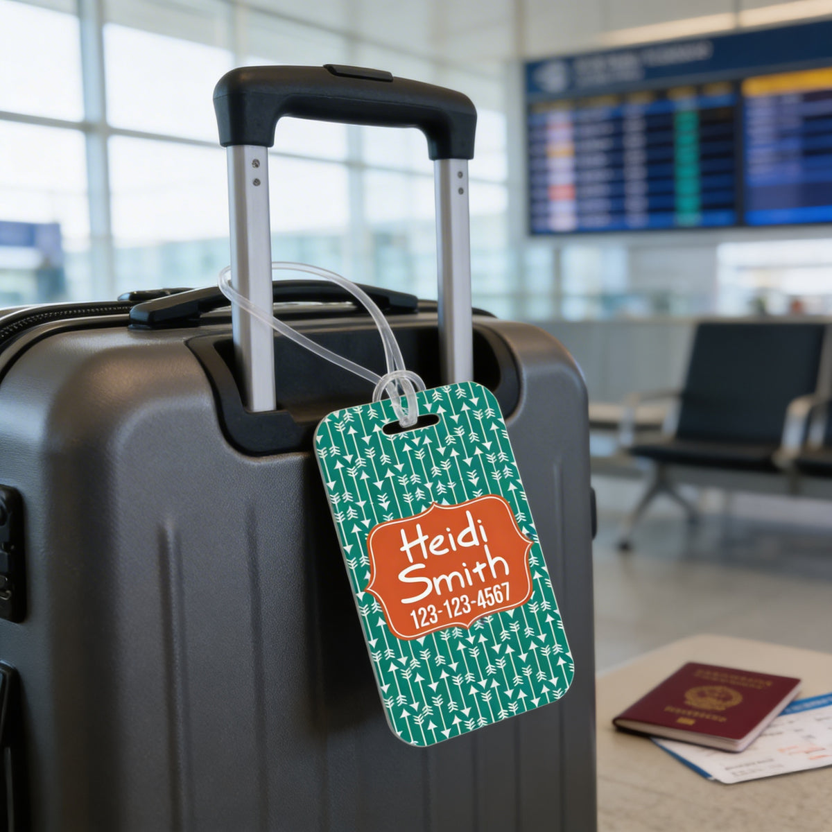 A black rolling suitcase with a green and orange luggage tag attached, displaying the name 'Heidi Smith' and a phone number.