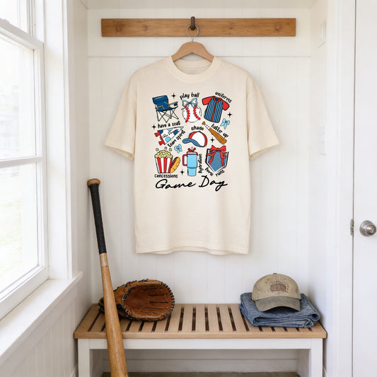 A white t-shirt with a colorful graphic design hanging on a wooden hanger in a hallway, accompanied by a baseball bat, glove, and hat.