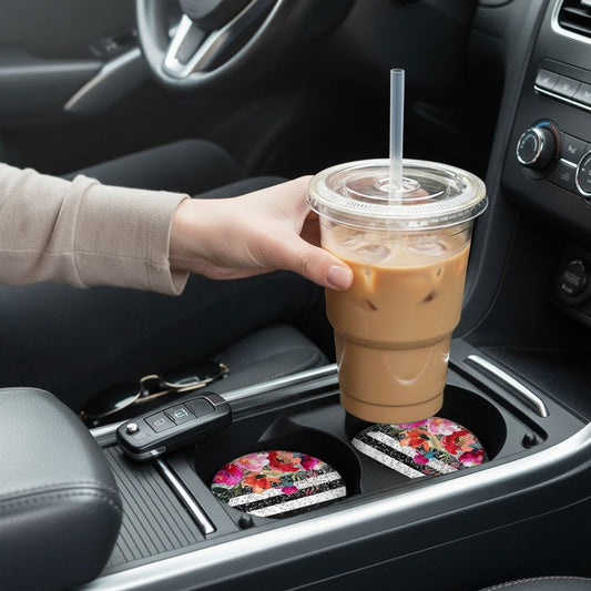 A person's hand is holding a plastic cup with a straw, which is placed in the car's center console.