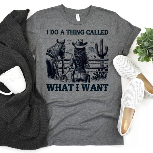 a gray t-shirt with a graphic design depicting a woman in cowboy attire, holding a horse, and the text "I DO A THING CALLED WHAT I WANT" printed on it.