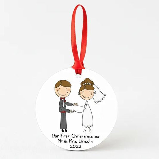 A round ornament with a red ribbon, depicting a cartoon illustration of a bride and groom. The text below the illustration reads "Our first Christmas as Mr. & Mrs. Lincoln", indicating the ornament is a personalized gift for the newlywed couple.