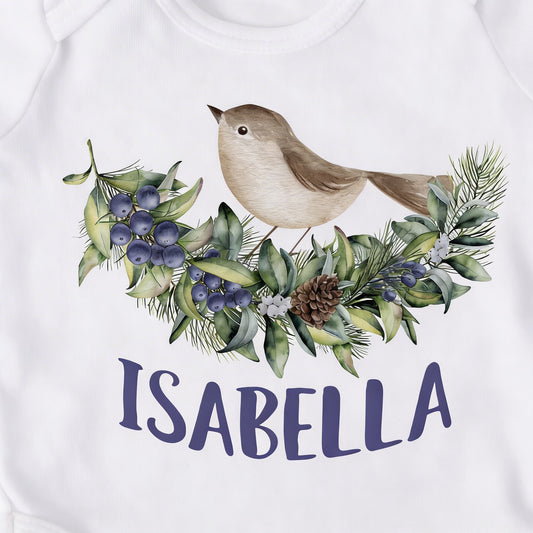 A white t-shirt with a printed design of a bird perched on a branch with berries and pine needles. The name "ISABELLA" is written below the design.