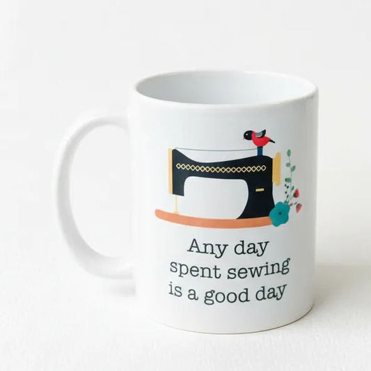 A white ceramic mug with a black sewing machine illustration and the text "Any day spent sewing is a good day" printed on it.