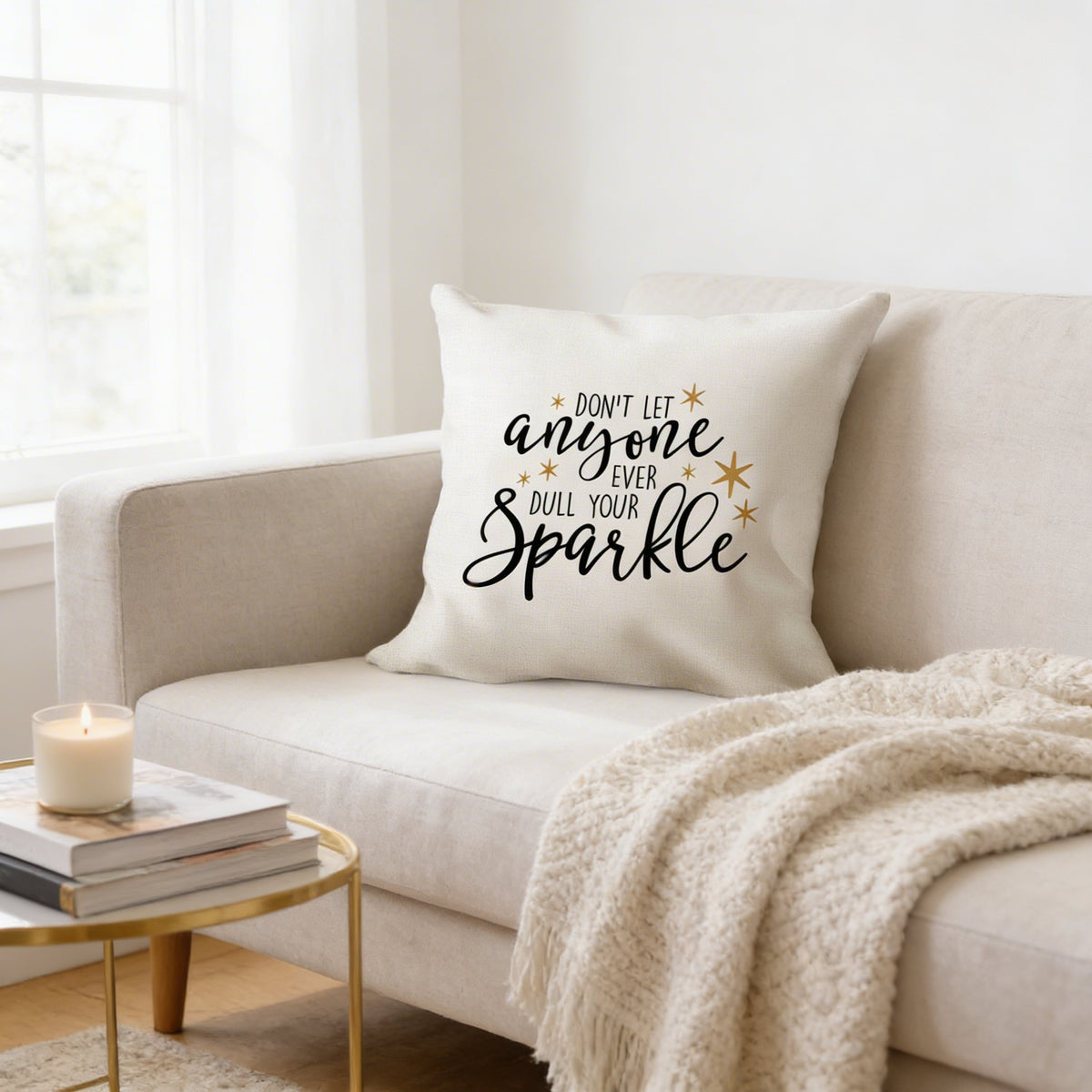 a cozy living room with a white couch, a stack of books, and a candle on a small table. The centerpiece of the image is a white throw pillow with a motivational quote, "Don't let anyone ever dull your sparkle", accompanied by a star design.