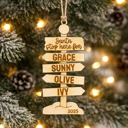 A wooden ornament hanging on a Christmas tree, featuring a directional sign with the names of the five daughters of Santa Claus.