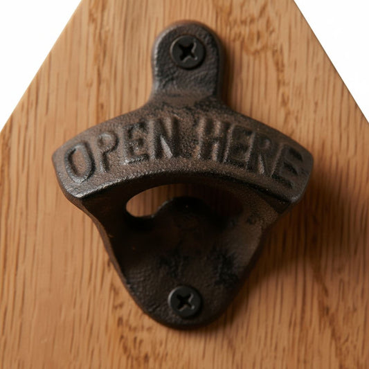 A close-up image of a metal bottle opener with the word "OPEN HERE" engraved on it, mounted on a wooden surface.