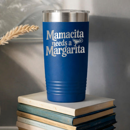 A blue tumbler with the text "Mamacita needs a Margarita" printed on it, sitting on top of a stack of books.
