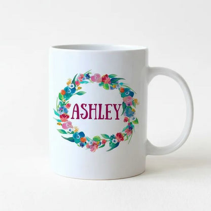 A white ceramic mug with a floral wreath design and the name "Ashley" printed on it.