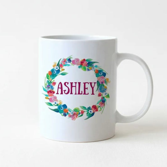 A white ceramic mug with a floral wreath design and the name "Ashley" printed on it.