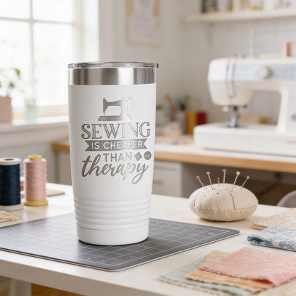 A white tumbler with a silver lid, featuring a sewing-themed design and text, sits on a table in a sewing workshop.