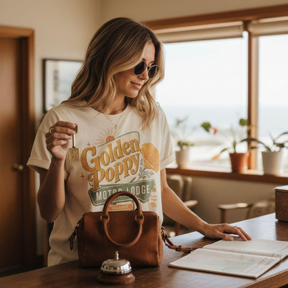 A woman in a white t-shirt with a graphic design holding a key stands in a room with a wooden table, a brown purse, and a bell.