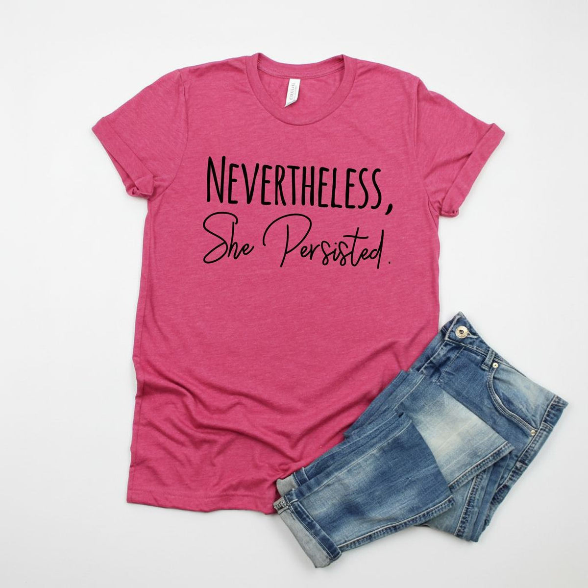 A pink t-shirt with the text "NEVERTHELESS, She Persisted" printed on it, along with a pair of blue jeans.