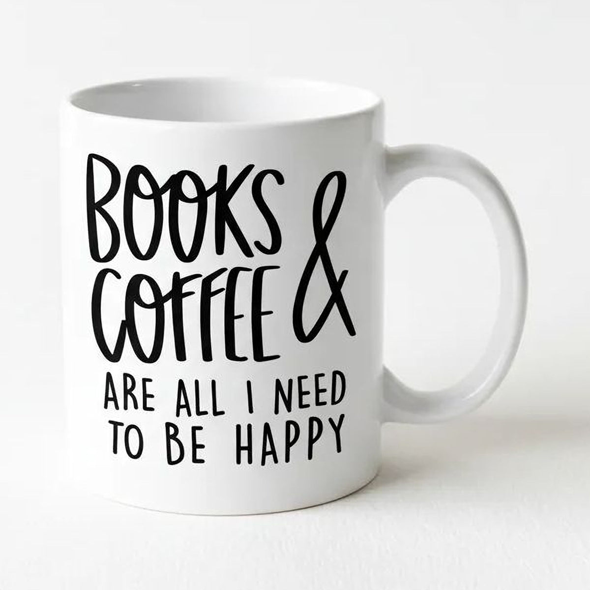 A white ceramic mug with black text that reads "BOOKS & COFFEE ARE ALL I NEED TO BE HAPPY".