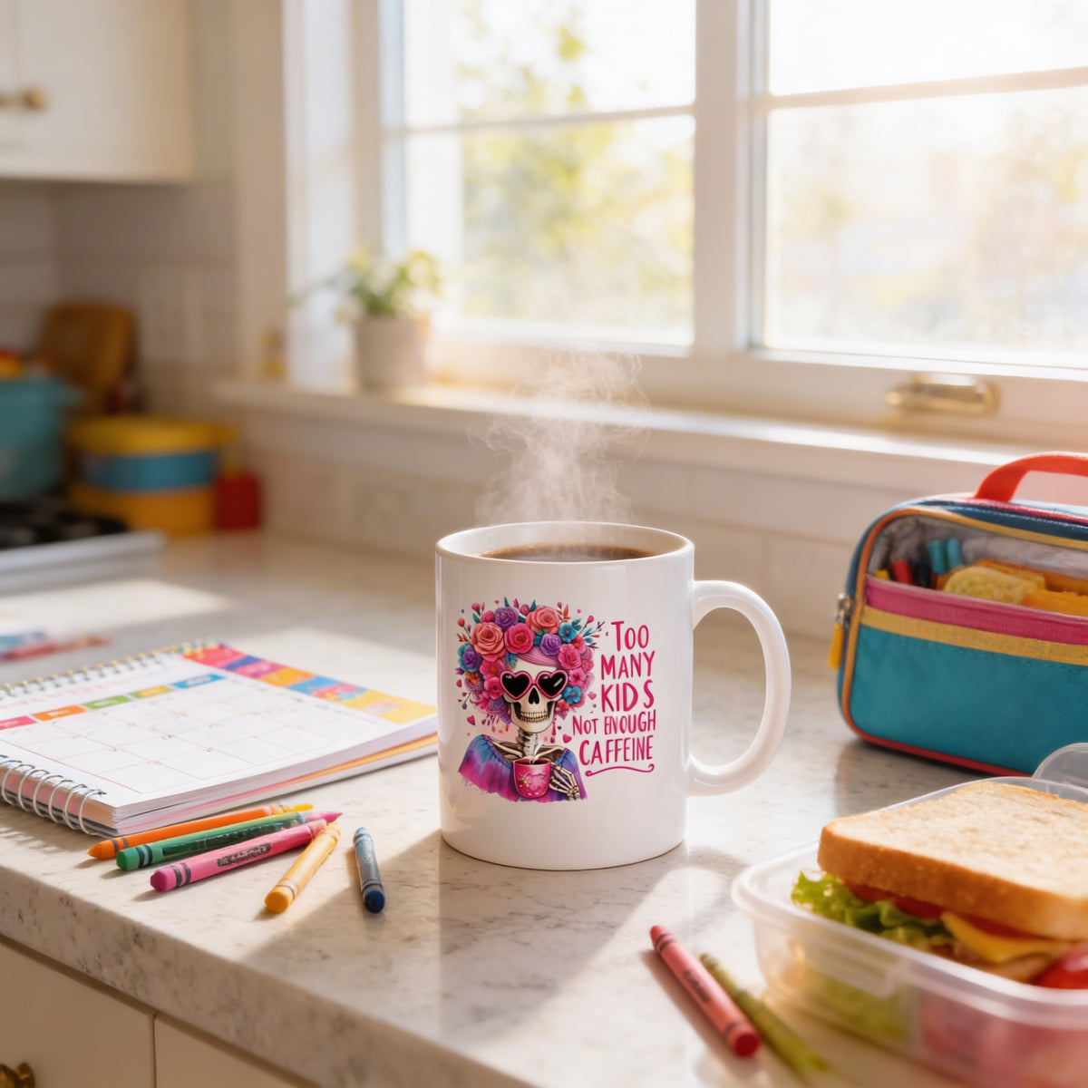 A white mug with a colorful design and text, placed on a kitchen counter next to a notebook, a sandwich, and some crayons.