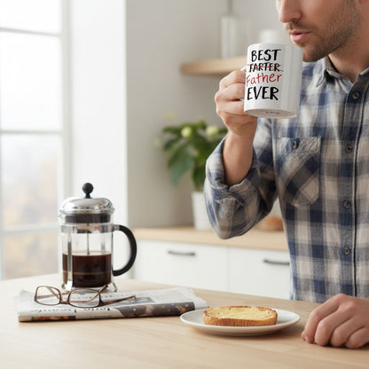 A man in a plaid shirt is sitting at a table, holding a coffee mug with the text "BEST TARTER FATHER EVER" printed on it. The table also has a French press coffee maker, a newspaper, and a plate with toast.