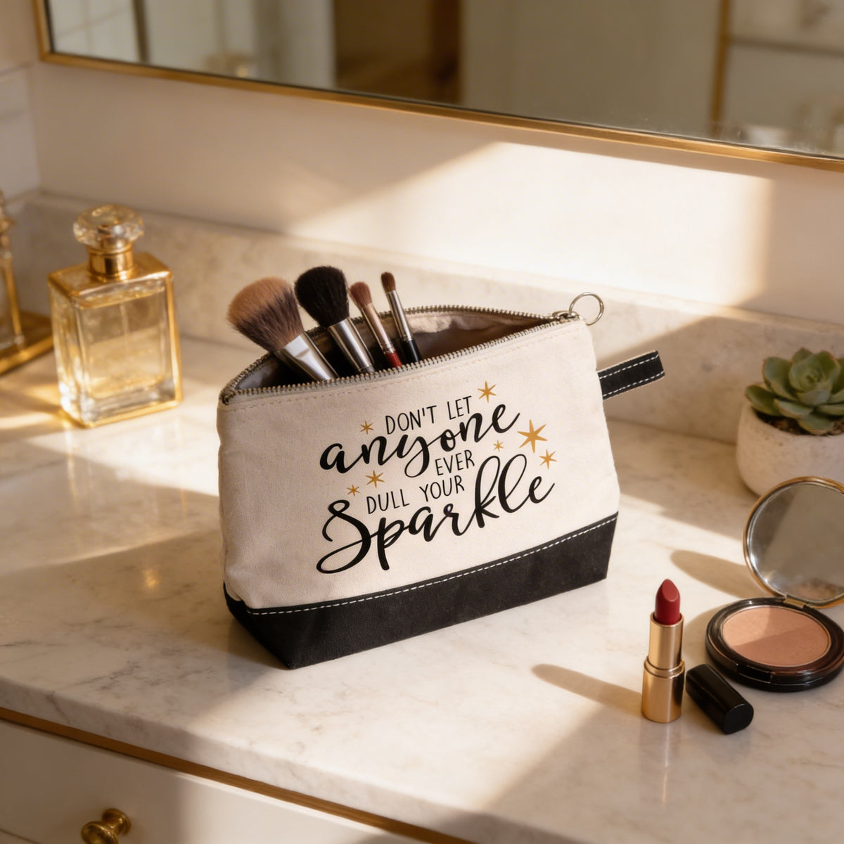 A makeup bag with a motivational quote, "Don't let anyone dull your sparkle", sits on a bathroom counter surrounded by makeup products and a mirror.