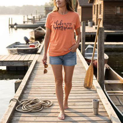 A woman wearing a t-shirt with the text "Lake is my happy place" walks on a wooden dock, holding a paddle and sunglasses.