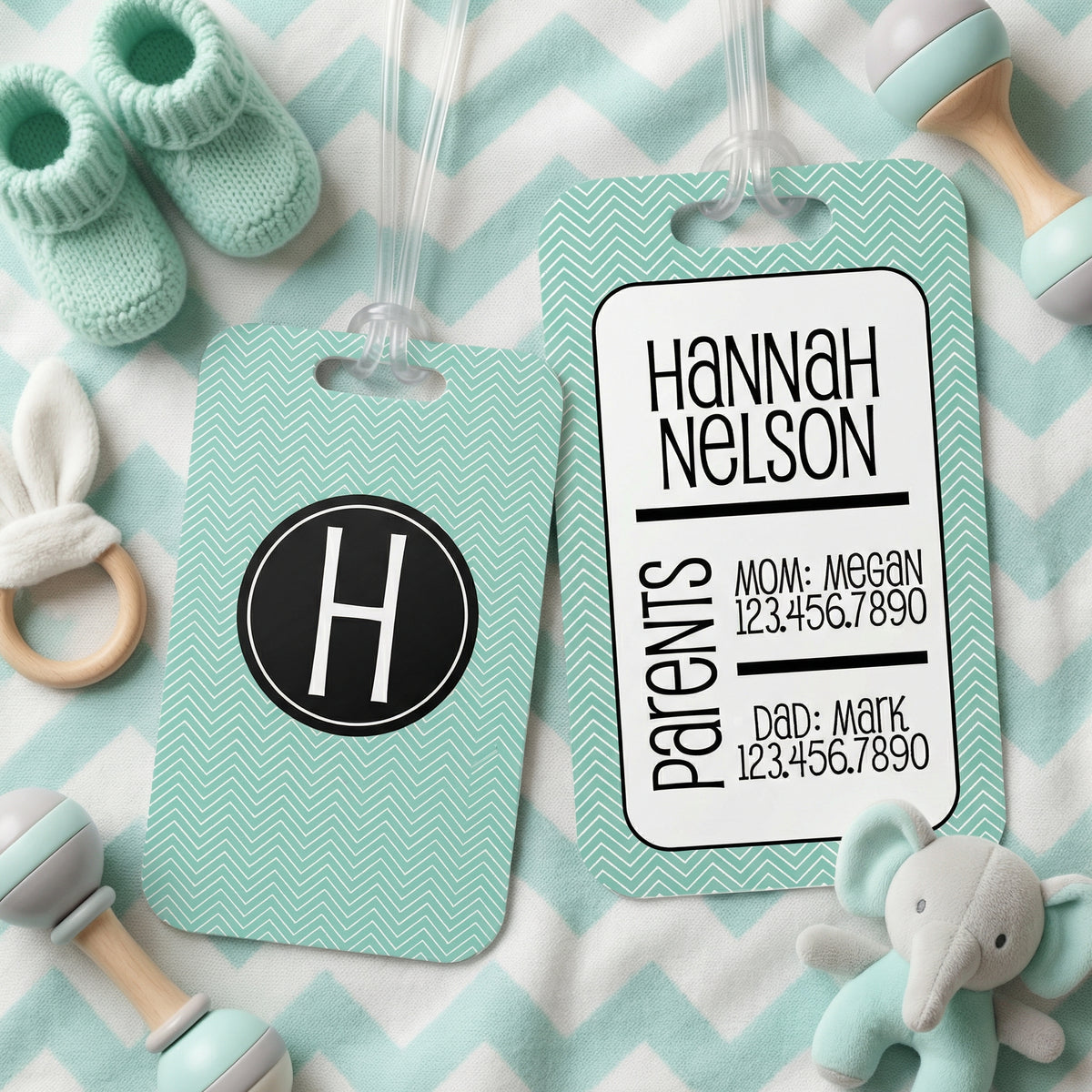 a baby tag with a monogrammed name, a baby bootie, and a stuffed elephant toy, all arranged on a chevron-patterned background.
