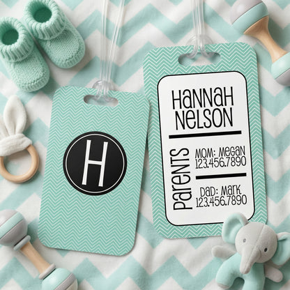 a baby tag with a monogrammed name, a baby bootie, and a stuffed elephant toy, all arranged on a chevron-patterned background.