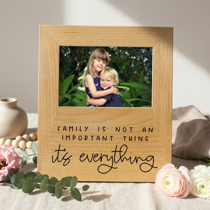 A wooden picture frame with a photo of two children inside, surrounded by flowers and greenery. The frame has a message that says "Family is not an important thing, it's everything".