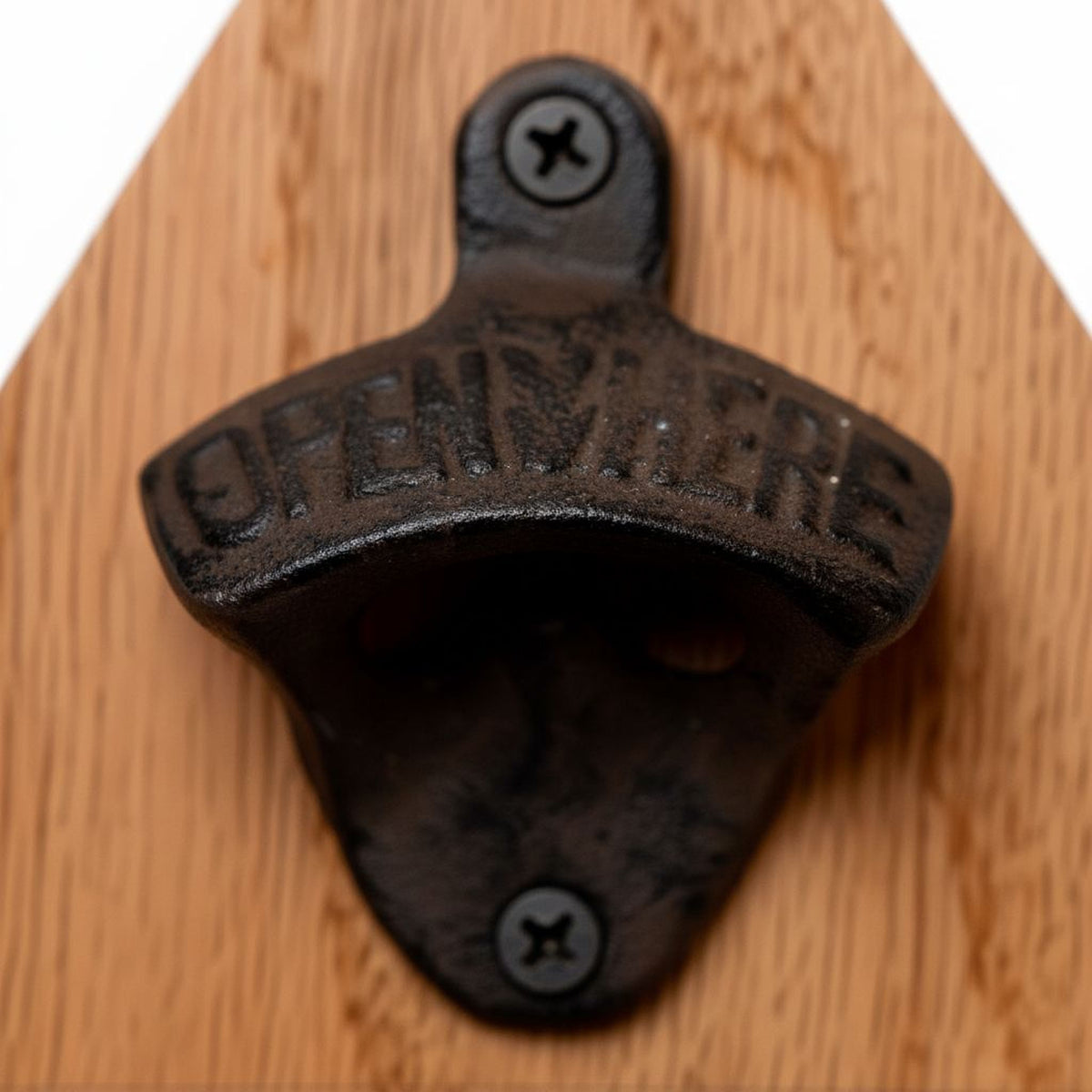 A close-up image of a black metal bottle opener with the word "OPEN HERE" engraved on it, mounted on a wooden surface.