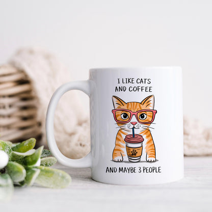 A white mug with an illustration of a cat wearing glasses and holding a coffee cup, accompanied by the text "I LIKE CATS AND COFFEE AND MAYBE 3 PEOPLE".