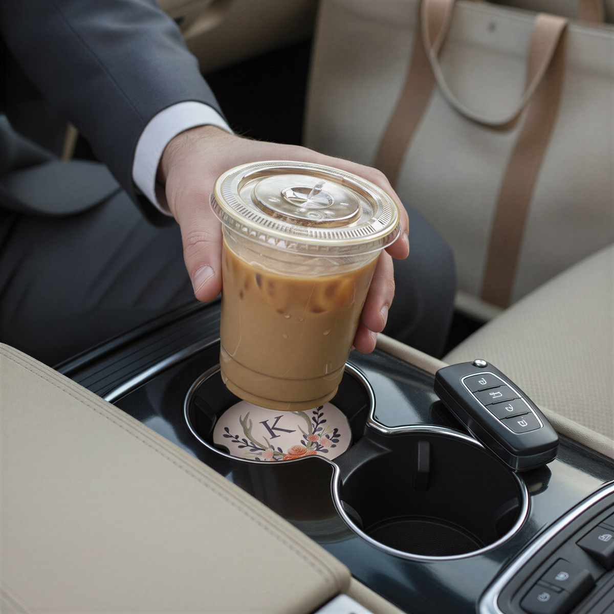 A person's hand is holding a cup of iced coffee in the car's cup holder.