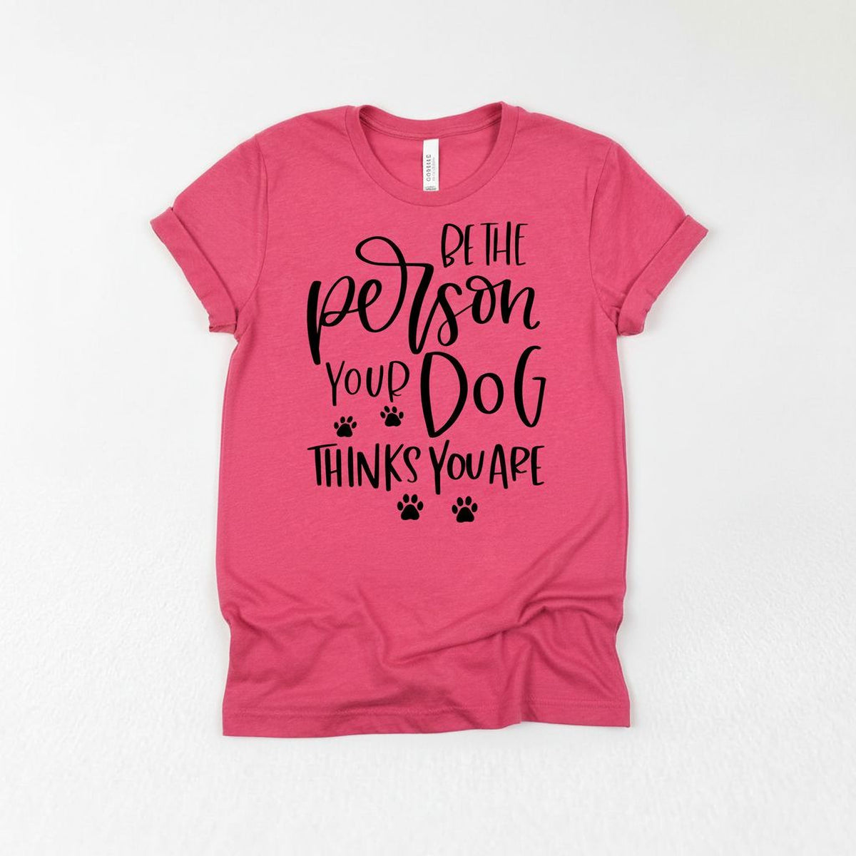 A pink t-shirt with a printed text that reads "Be the person your dog thinks you are".