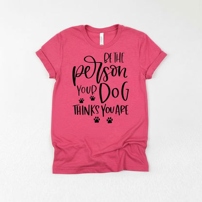 A pink t-shirt with a printed text that reads "Be the person your dog thinks you are".