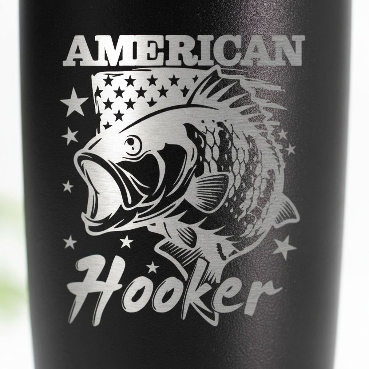a black tumbler with a silver design of a fish and stars, along with the text "American Hooker" printed on it.