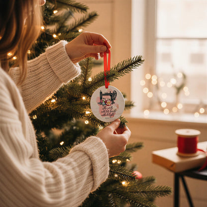 A person in a white sweater is decorating a Christmas tree with a round ornament featuring a sewing machine and the text "I love you with all my heart".