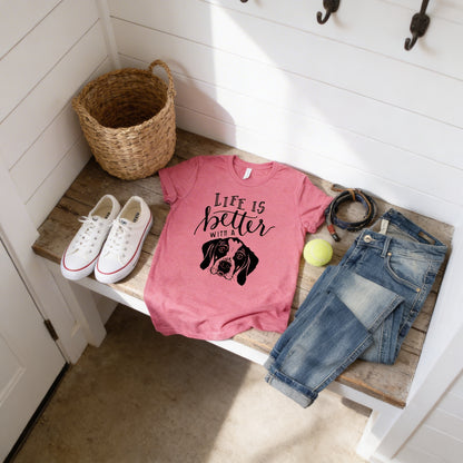 a pink t-shirt with a dog graphic, a pair of jeans, a pair of white sneakers, a woven basket, and a tennis ball on a wooden bench.