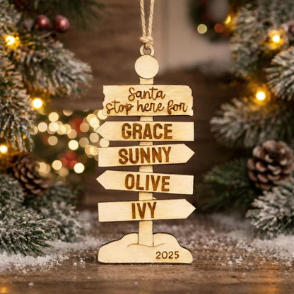 A wooden ornament with a directional sign, featuring the names of five people, is displayed in front of a Christmas tree with twinkling lights.