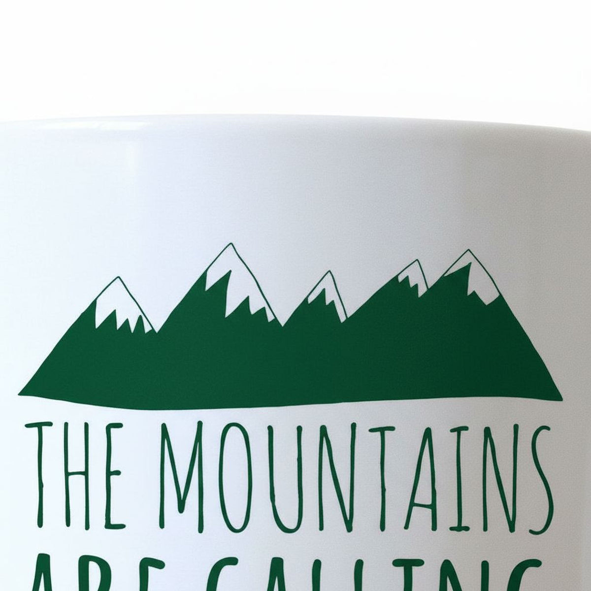A white mug with a green mountain range design and the text "THE MOUNTAINS ARE CALLING" printed on it.