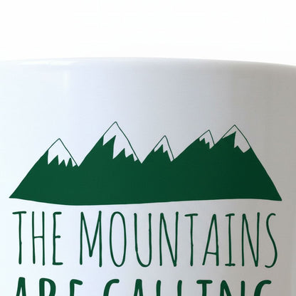 A white mug with a green mountain range design and the text "THE MOUNTAINS ARE CALLING" printed on it.