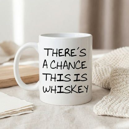 A white ceramic mug with black text printed on it, sitting on a surface with a beige cloth and a wooden cutting board in the background.