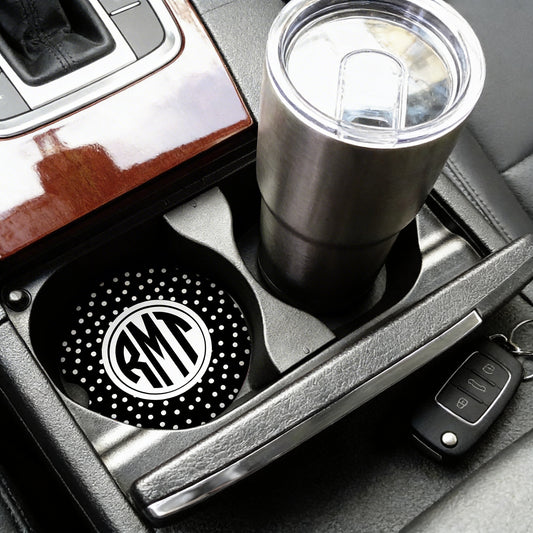 A stainless steel tumbler with a personalized monogrammed lid is placed in the car's cup holder, accompanied by a key fob.