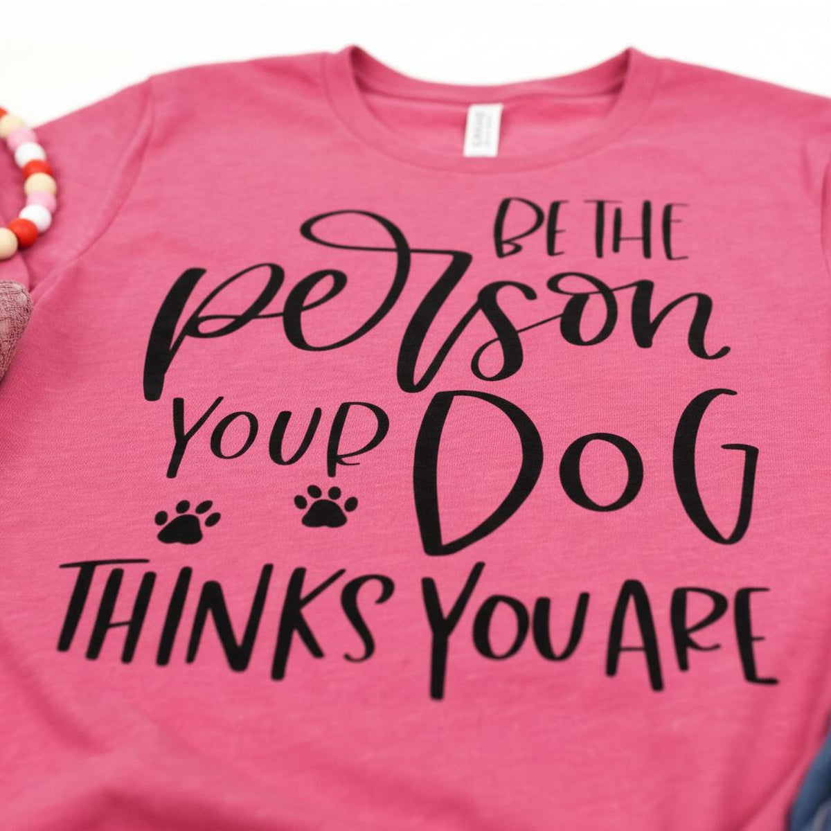 A pink t-shirt with the text "Be the person your dog thinks you are" printed on it.
