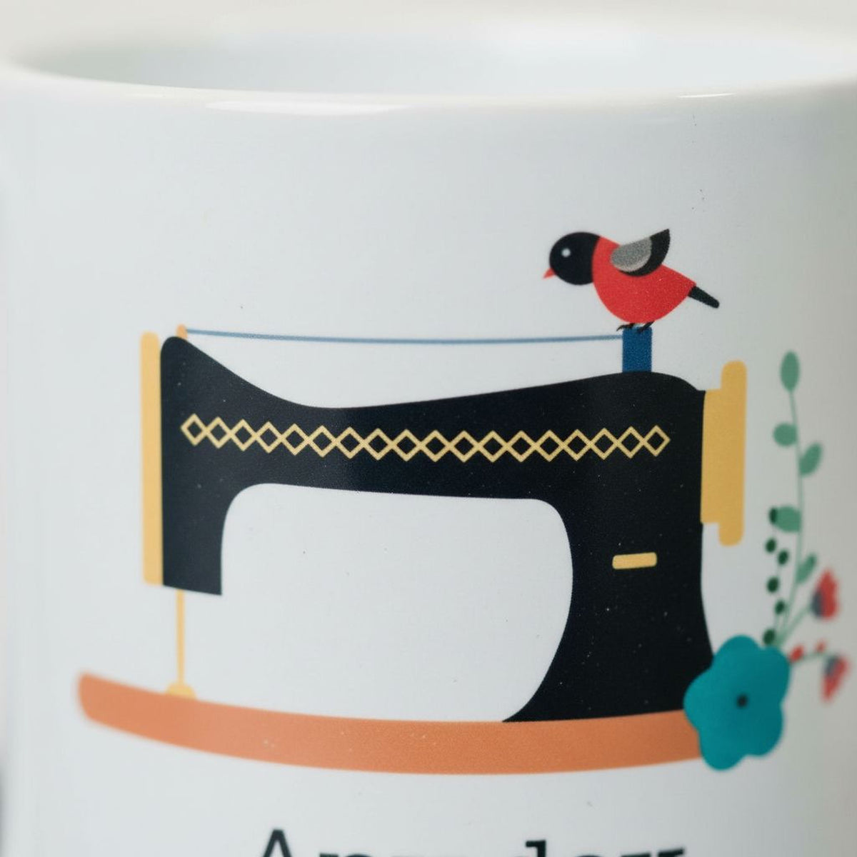 A close-up of a white mug with a black sewing machine and a red bird perched on it.