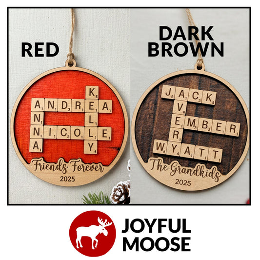 two wooden ornaments hanging on a string, each with a different color and design. The ornaments are shaped like a crossword puzzle with letters on the pieces, and they are labeled with the names of family members or friends.