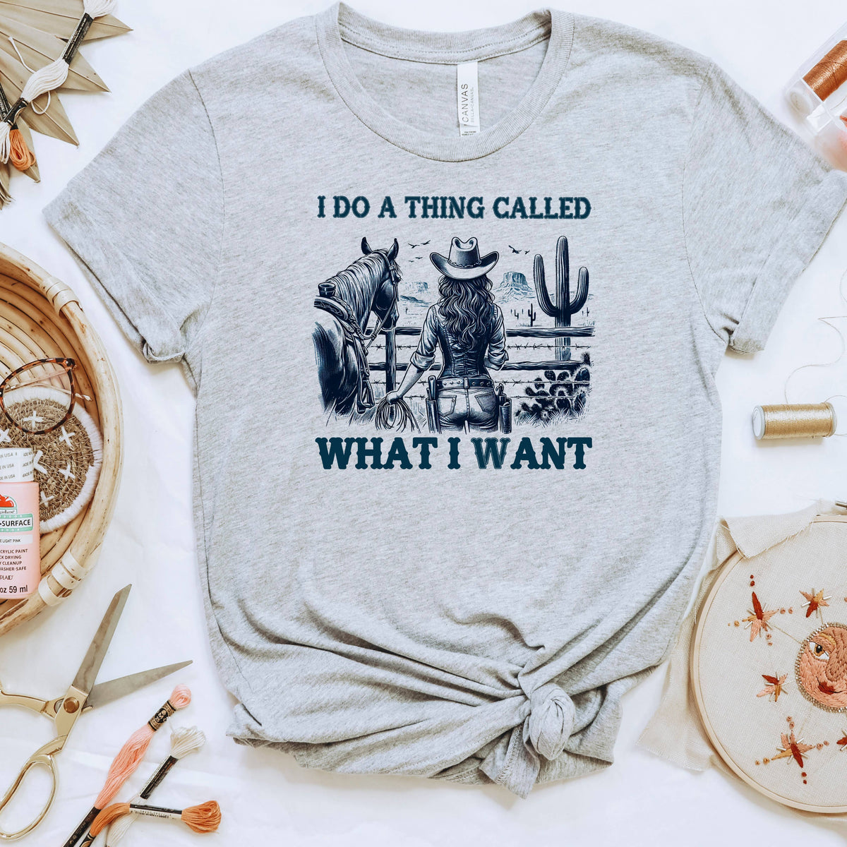 a grey t-shirt with a graphic design depicting a woman in a cowboy hat standing next to a horse, with the text "I DO A THING CALLED WHAT I WANT" printed on it.