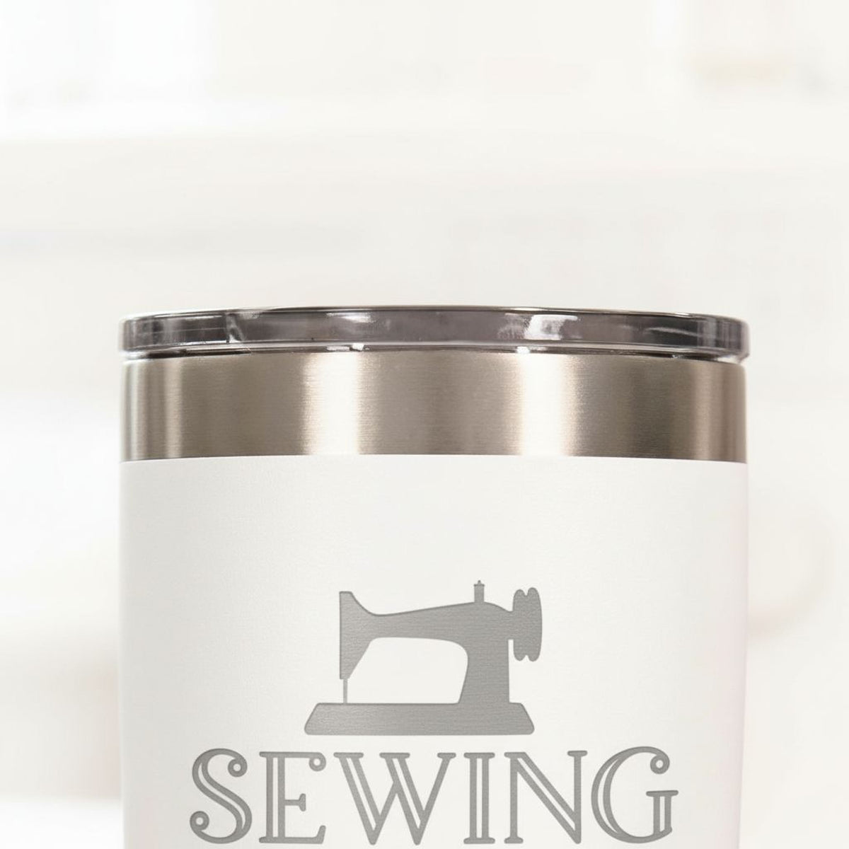A white tumbler with a silver lid, featuring a sewing machine logo printed on it.