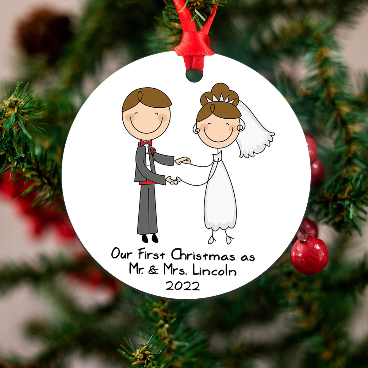 A white ornament with a red ribbon, featuring a cartoon illustration of a bride and groom holding hands.