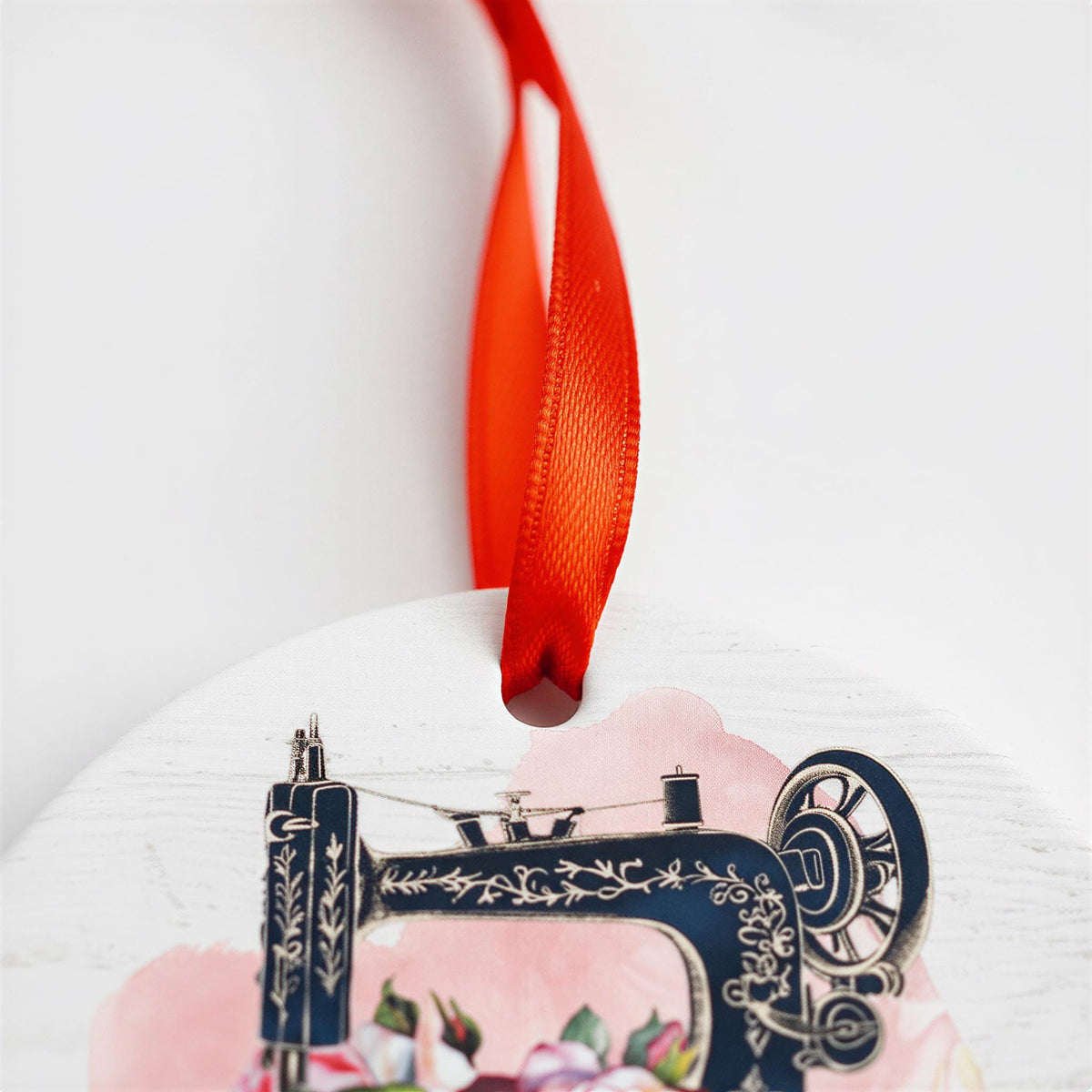 A decorative ornament featuring a sewing machine with a red ribbon tied around it.