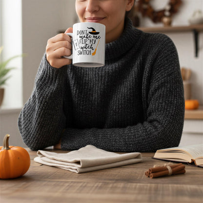 A woman in a gray sweater is sitting at a table, holding a mug with a humorous text on it, while a pumpkin and cinnamon sticks are visible on the table.