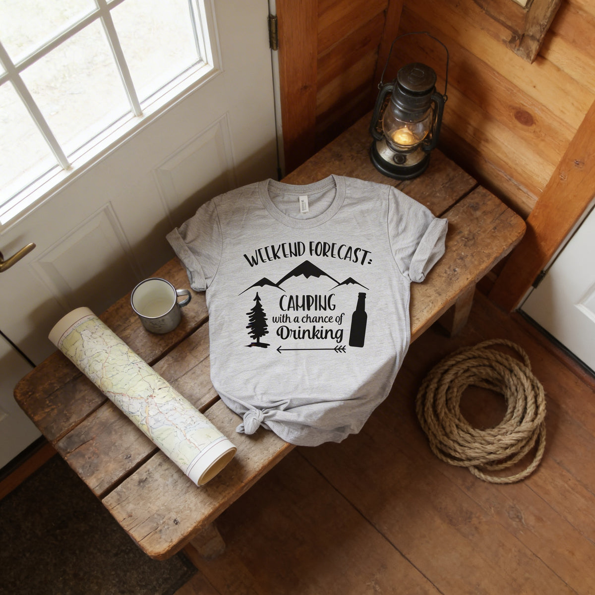 a gray t-shirt with a graphic design, a map, a lantern, and a rope on a wooden bench.