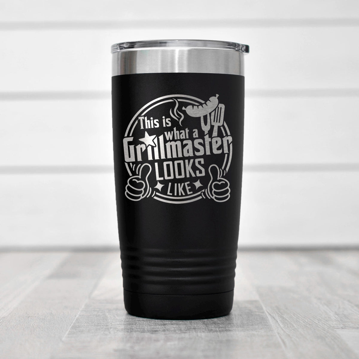 A black insulated tumbler with a silver lid, featuring a humorous text that says "This is what a Grillmaster looks like" along with a thumbs up symbol.