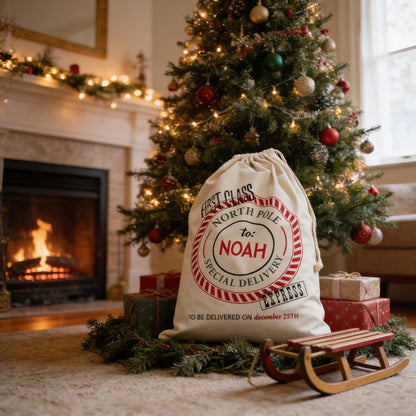 A Christmas tree decorated with ornaments and lights, with a bag labeled "First Class North Pole to Noah Special Delivery" placed on the floor in front of it.