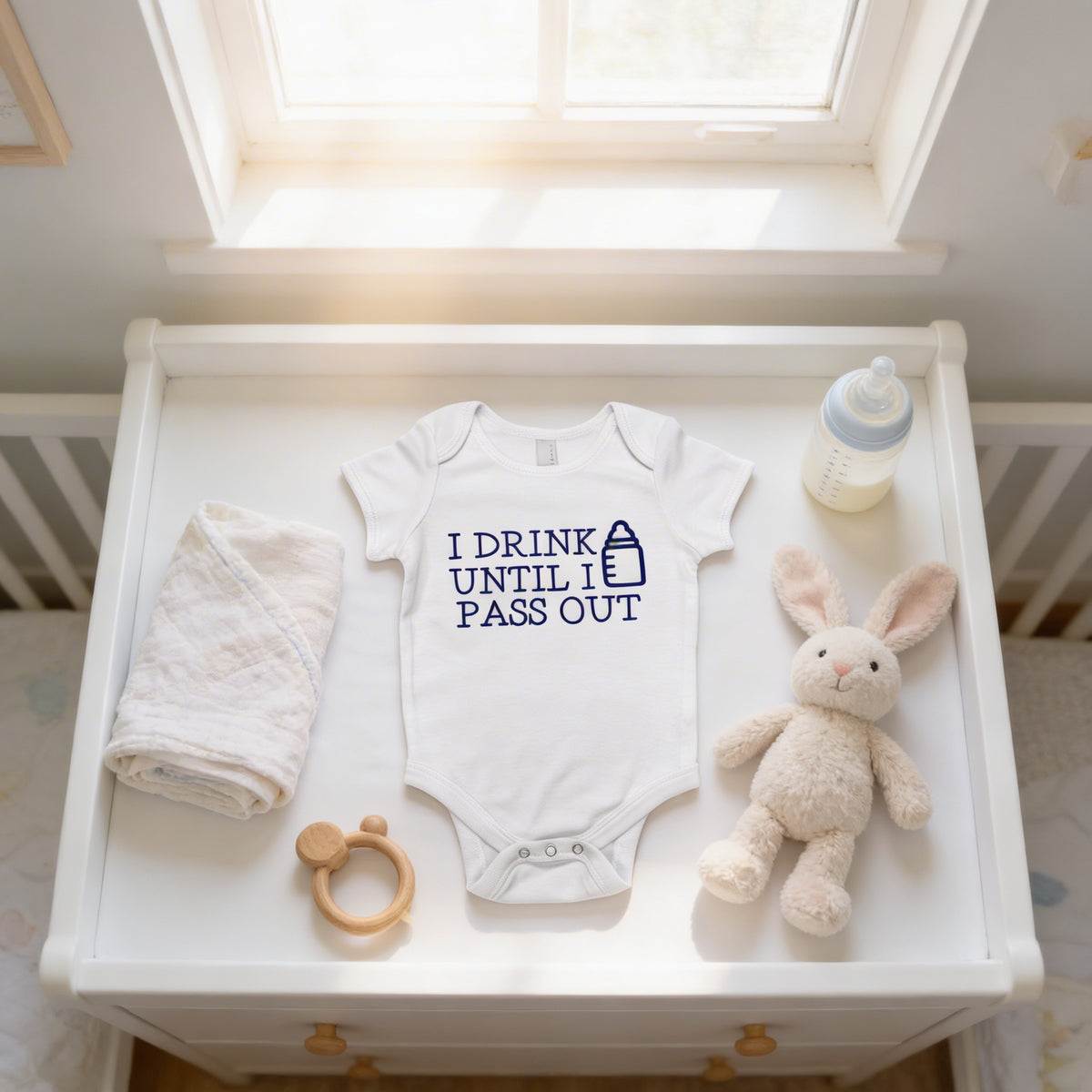 A white dresser with a baby's outfit, a bottle, a stuffed rabbit, and a wooden bib on it.